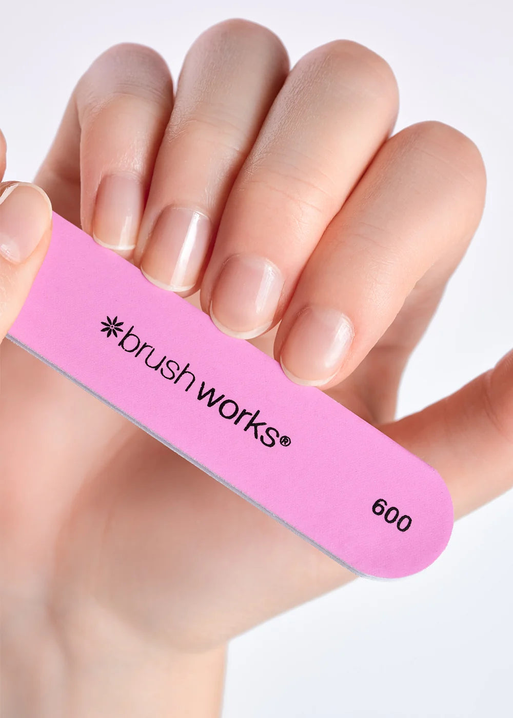 Hand holding a pink Brushworks 600-grit nail file